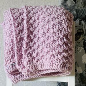 Handgestrickte Tagesdecke in Rosé, gefaltet auf weißem Stuhl, Detailansicht Strukturmuster