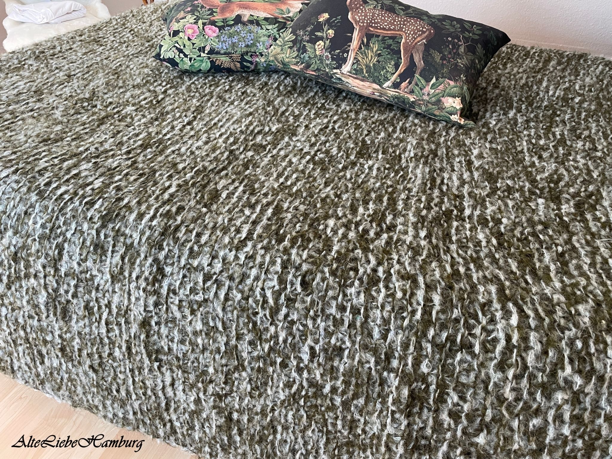 Handgestrickte Tagesdecke in Oliv-Grün-Meliert auf dem Bett mit Waldtier-Kissen – AlteLiebeHamburg