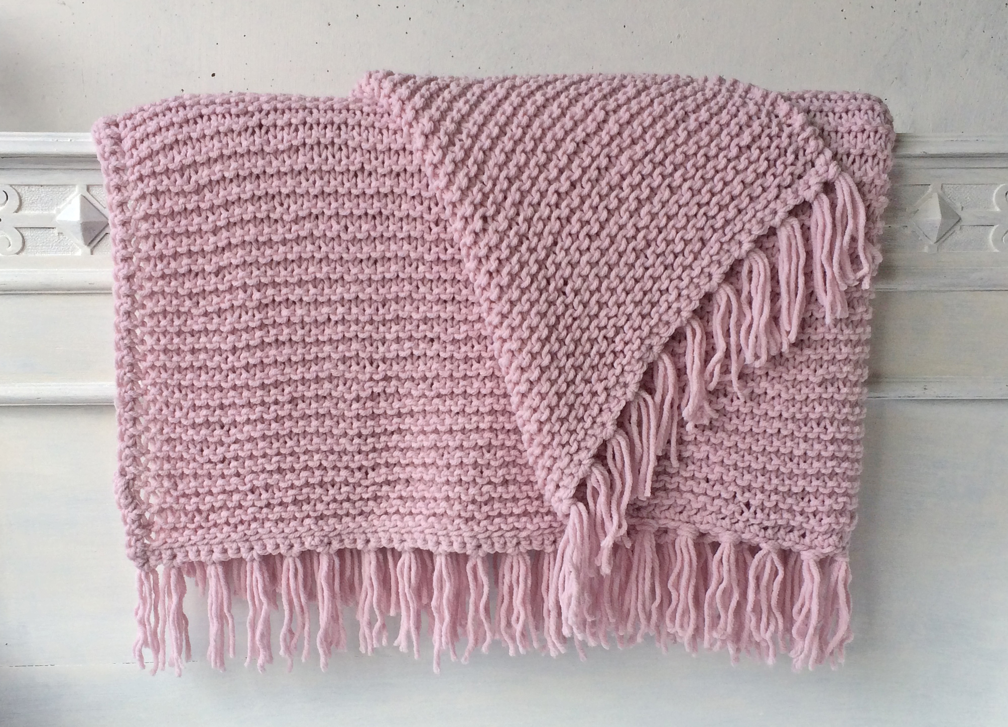 Handgestrickte Strickdecken mit Fransen in Rosé, aufgereiht auf einem weißen Bettgestell – AlteLiebeHamburg