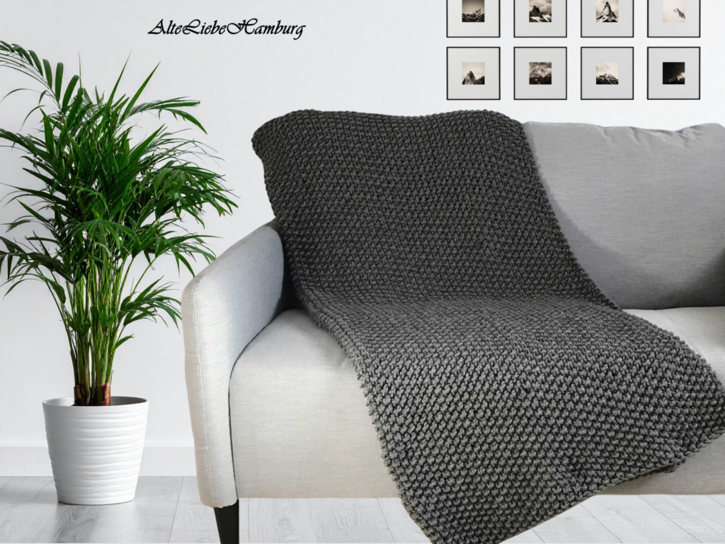 Wohnzimmer mit Zimmerpflanze und gerahmten Schwarz-Weiß-Bergfotos, graue Strickdecke über hellem Sessel drapiert – AlteLiebeHamburg