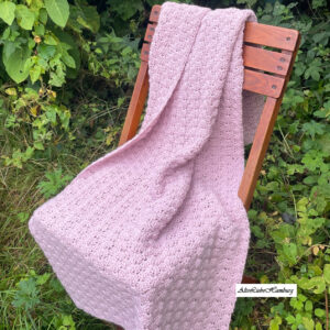 Handgehäkeltes altrosa Plaid aus Wolle, über eine Stuhllehne drapiert im Garten