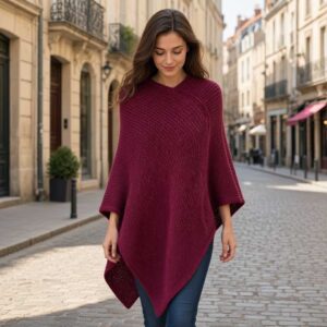 Eine dunkelhaarige Frau geht eine Straße entlang und trägt einen Poncho in Bordeaux Farben.